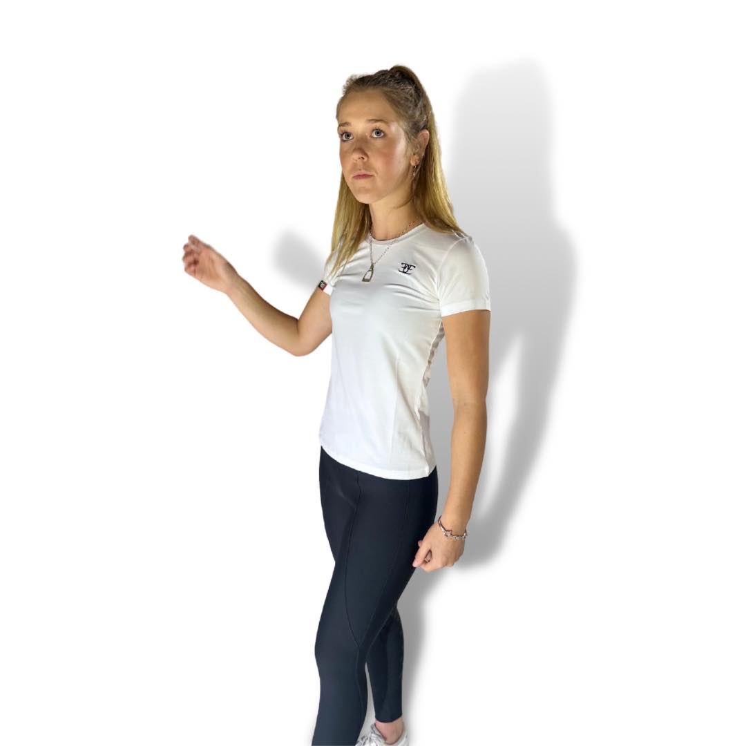 Woman in a white casual tee and dark pants, posing with one arm raised