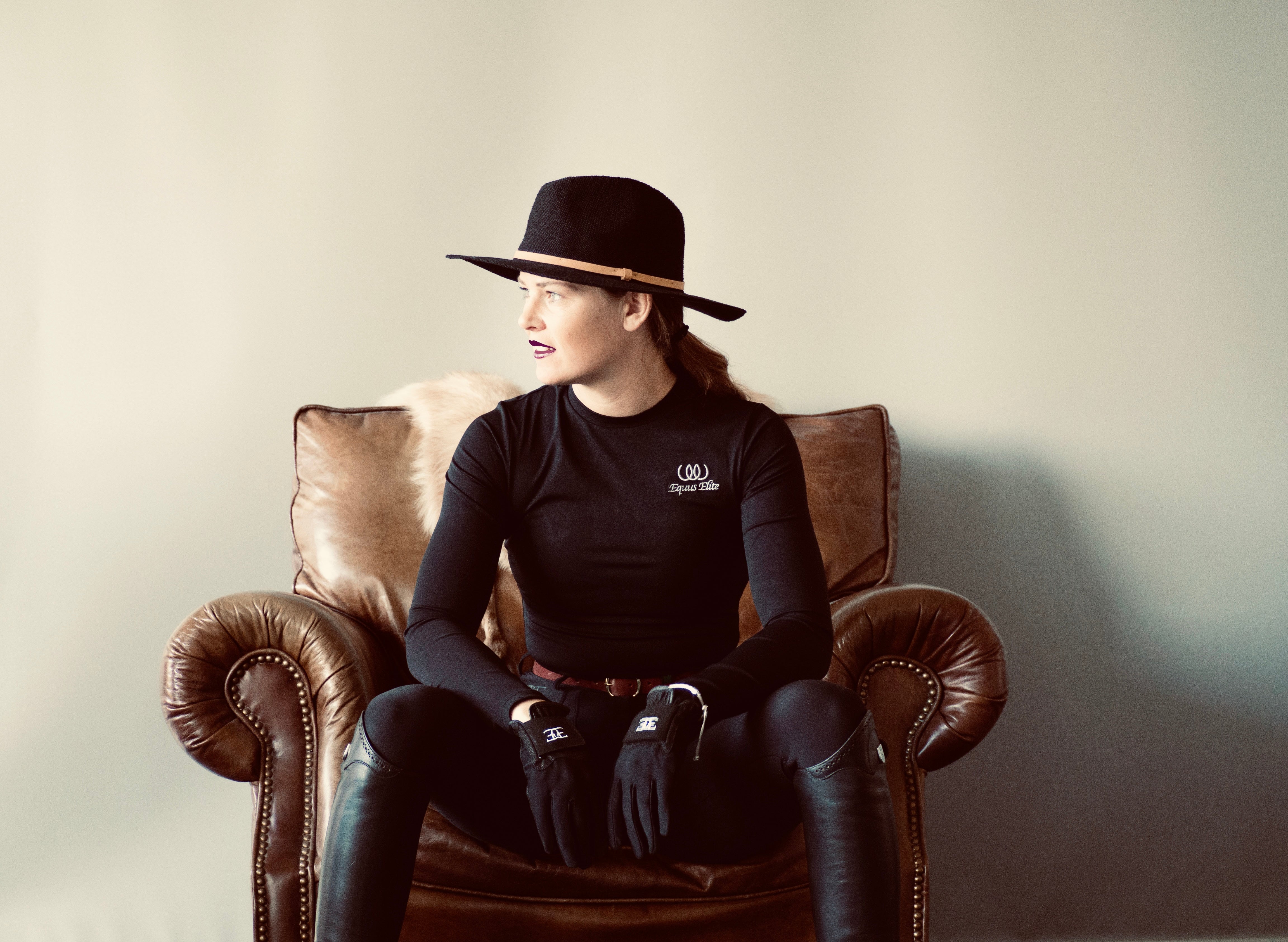 Woman in black outfit and hat showcasing Black Long Sleeved X-training shirt for riding