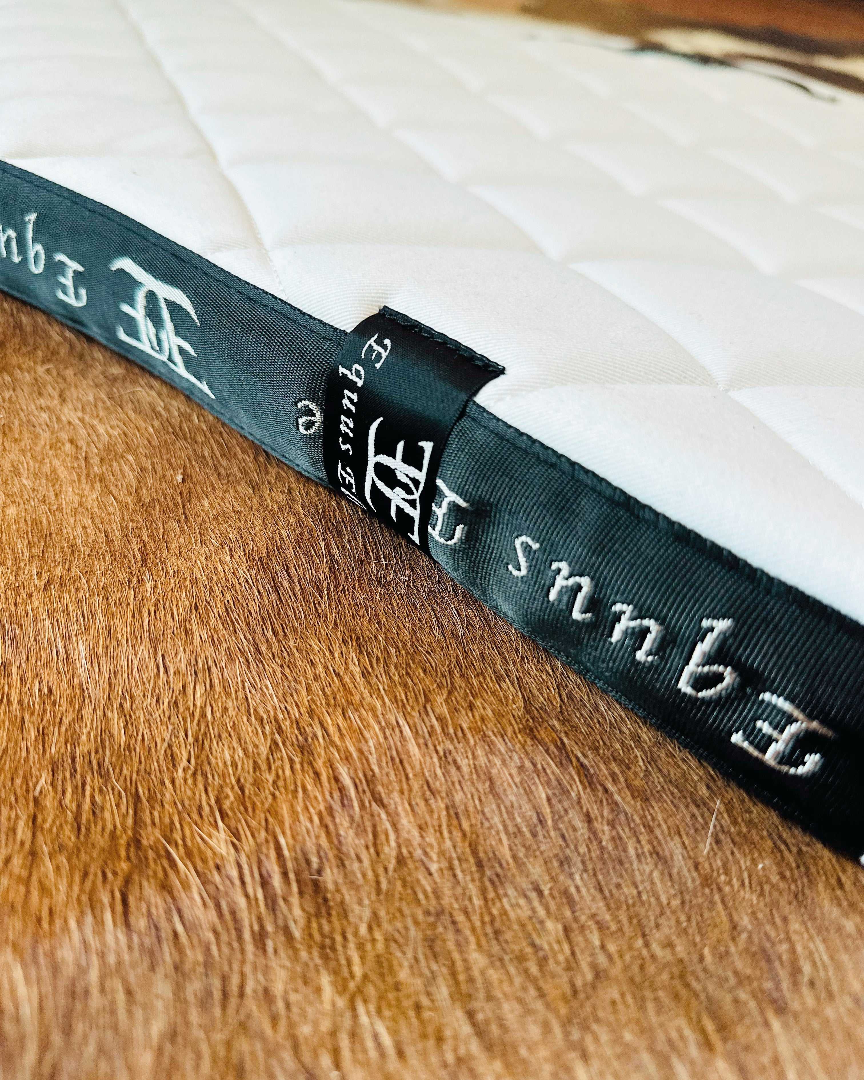 Dark green leather-bound book with ornate spine lettering next to Equus Elite Saddle Pad