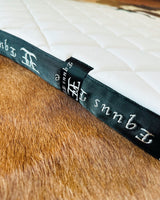Dark green leather-bound book with ornate spine lettering next to Equus Elite Saddle Pad