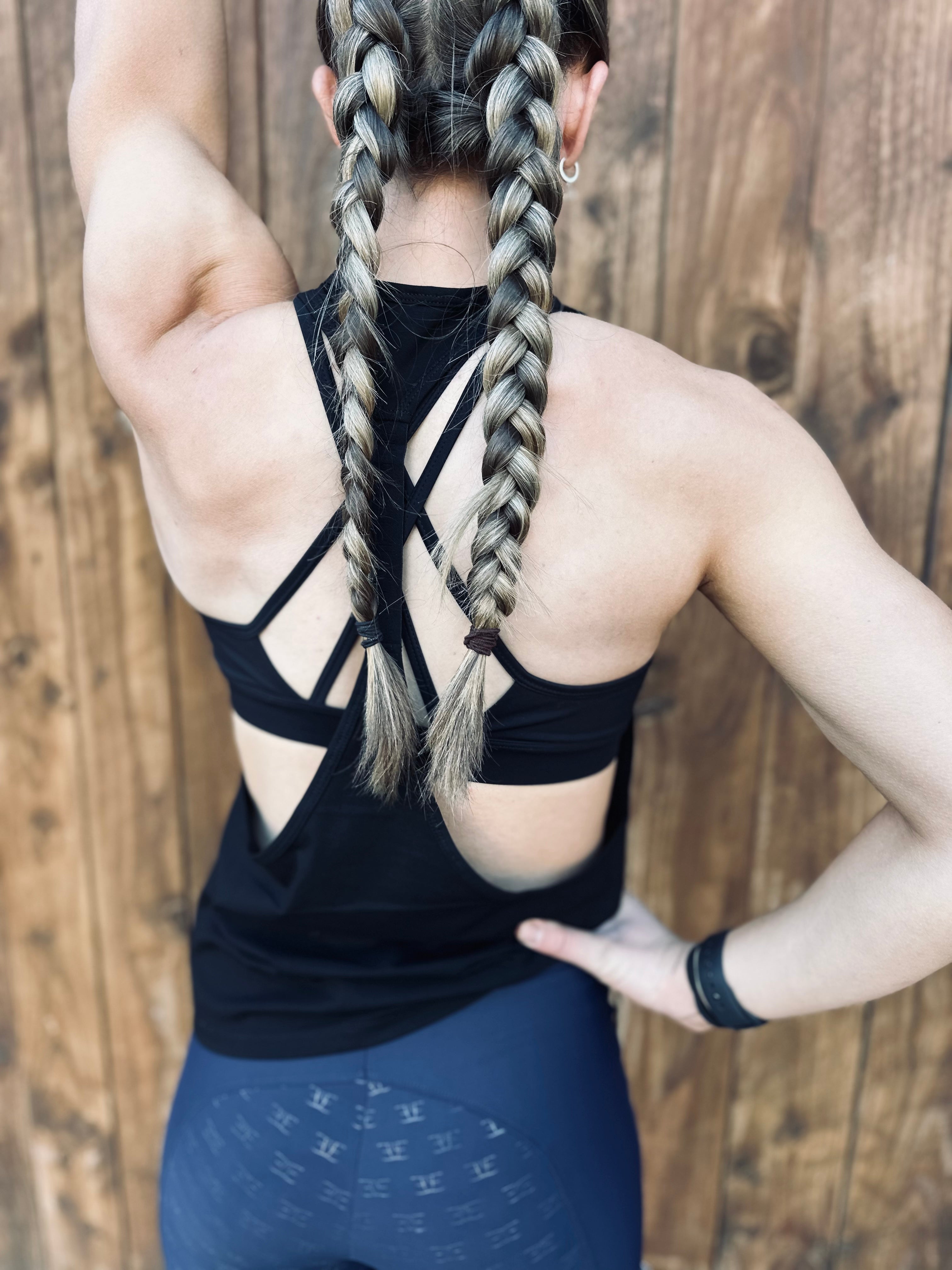 Person with long braided hair wearing a black drop arm fitness tank and blue leggings