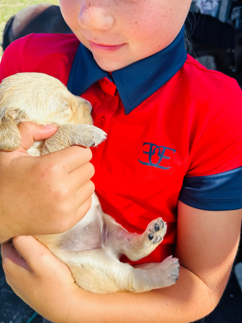 Puppy cuddled in arms, highlighting Kids Matching Polo in Red with breeches and riding tights