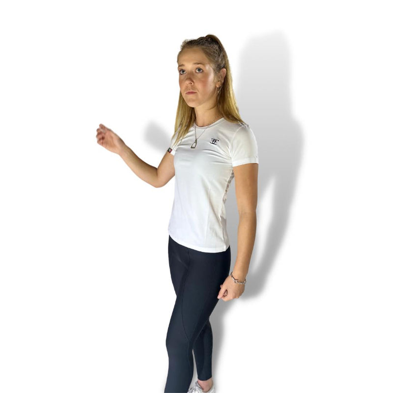Woman in a white casual tee and dark pants, posing with one arm raised