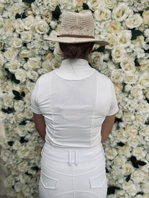 Person in a white show shirt and straw hat before a wall of white roses
