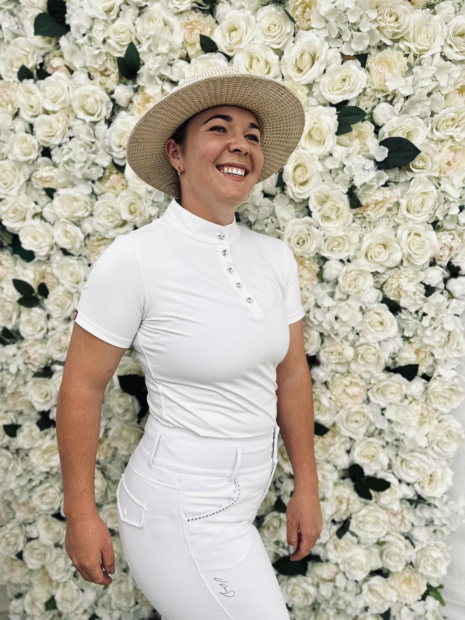 Woman in white Vanessa Way Breech and straw hat against floral backdrop